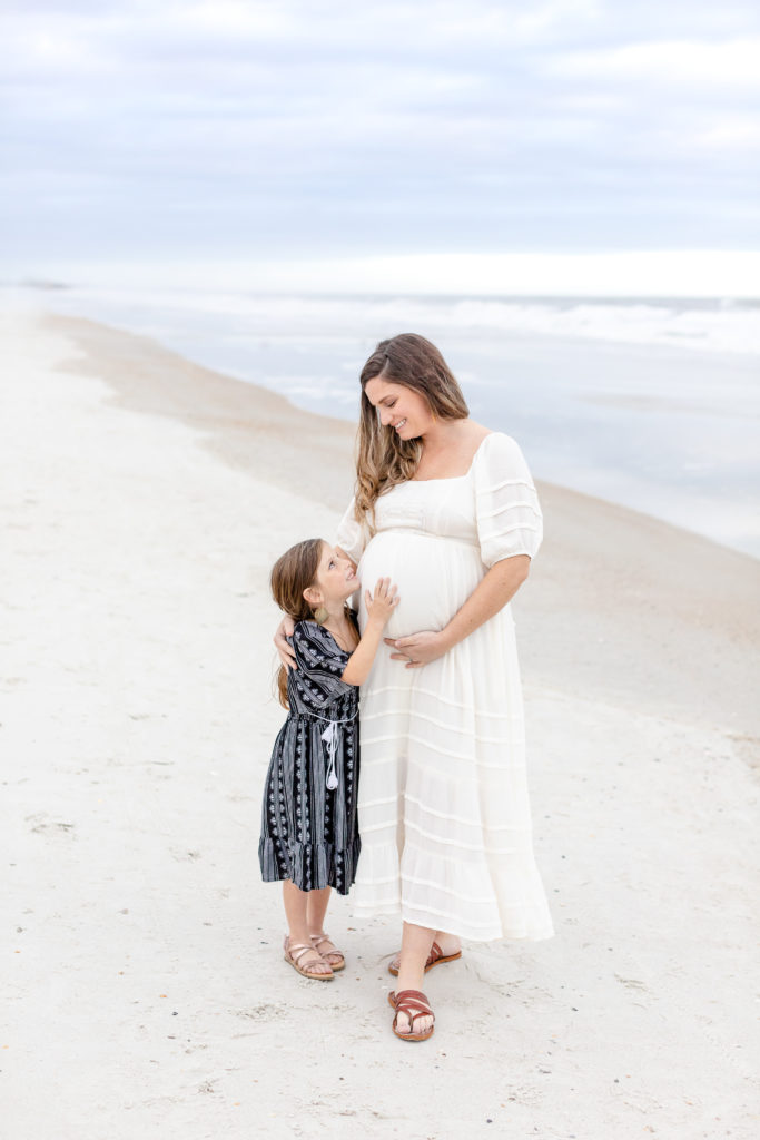 pregnant mom at maternity photo session on a beach with young daughter
