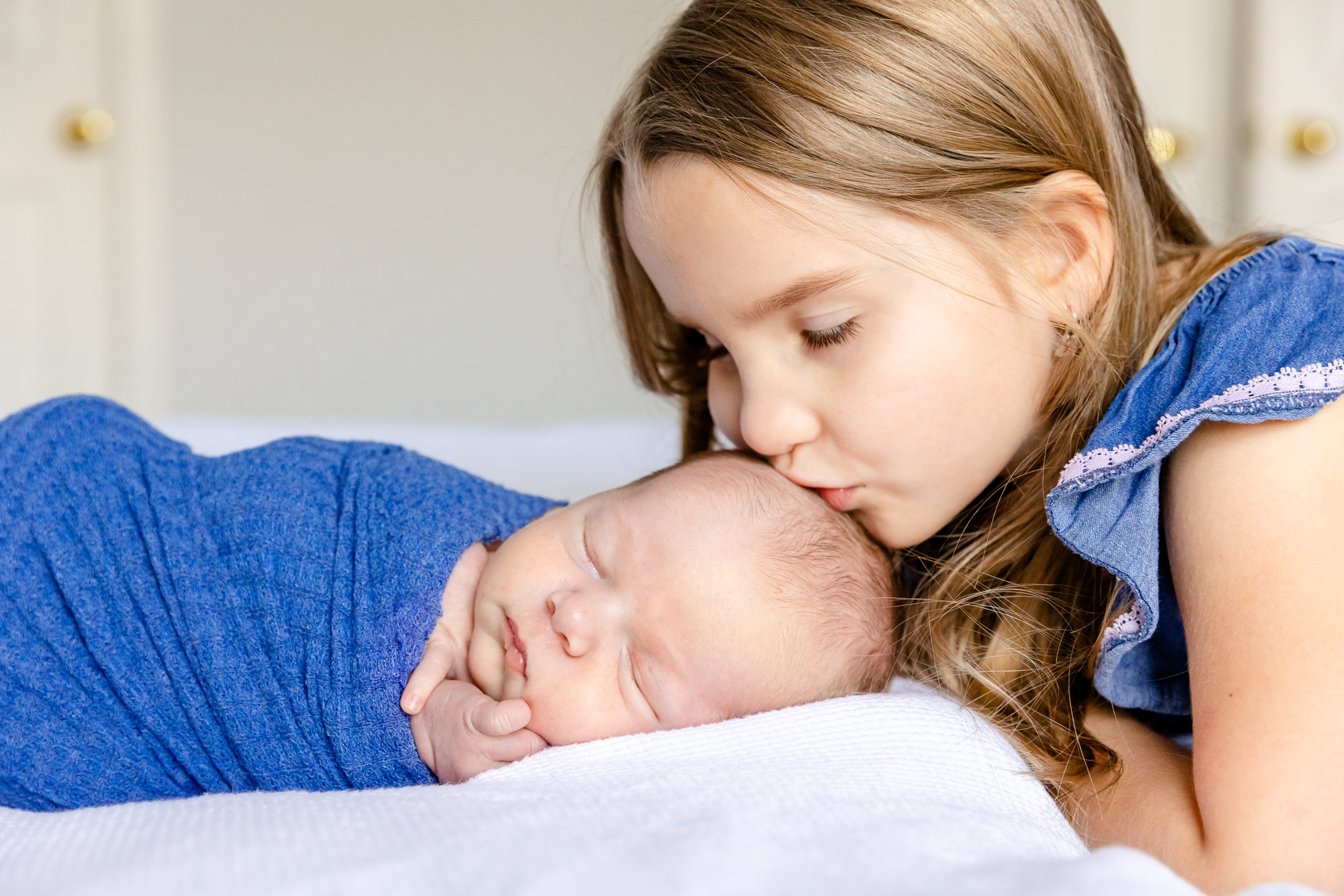 Big sister kissing baby brother's head during lifestyle newborn session
