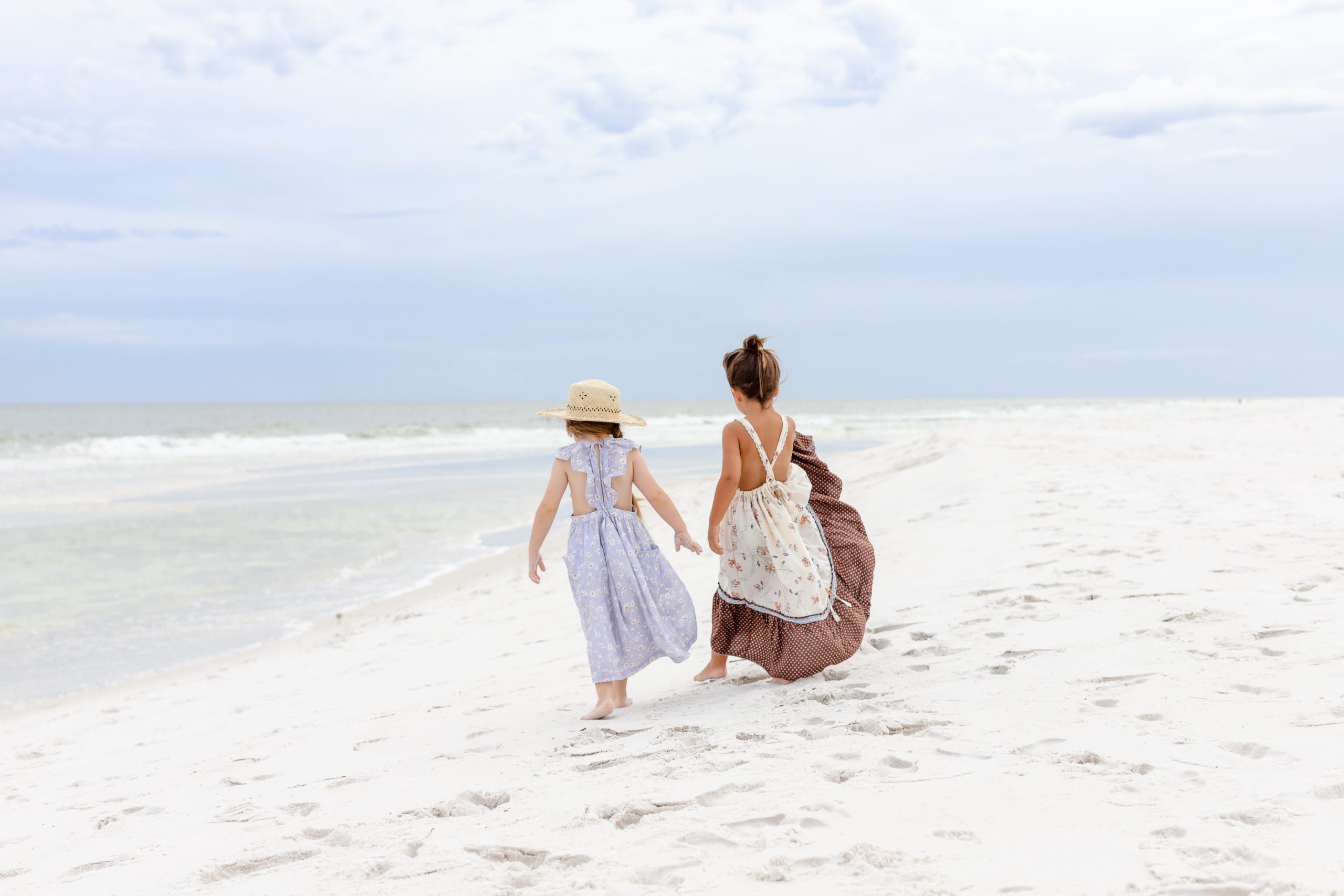 two girls are walking away from the camera down a white sand beach near Jacksonville Florida
